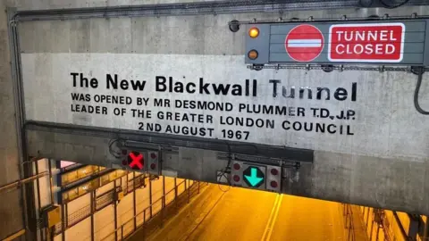 A sign above the road of the Blackwall Tunnel which says it was opened by the leader of the Greater London Council in August 1967