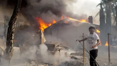 A man sprays water on a house destroyed from the Eaton Fire in the Altadena neighbourhood in PASADENA, CALIFORNIA. 