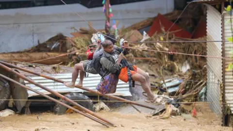 Two men hang from  zipline over floodwater