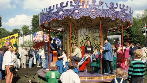 Children and adults pile onto  Keith Haring’s carousel in Hamburg as others watch on.