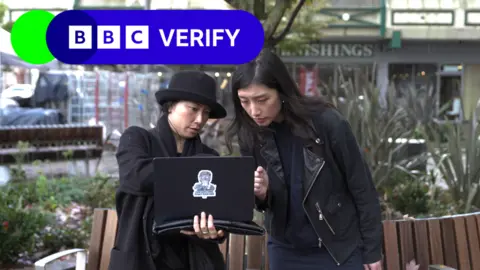 Two women standing outside looking intently at a laptop