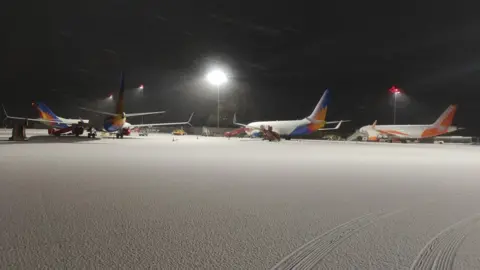 Charlie Haskayne A runway area covered in snow is shown at Bristol Airport, with four passenger planes visible in the background, two of them with Easyjet livery. There is a pair of tyre tracks made by a vehicle in the foreground