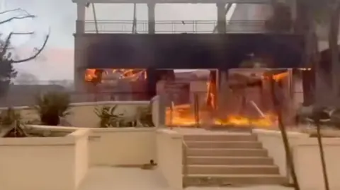 The ground floor of a burning school. The upstairs appears to have burnt away. As seen from the road