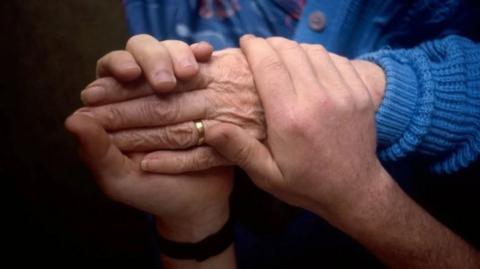 An elderly and young person holding hands