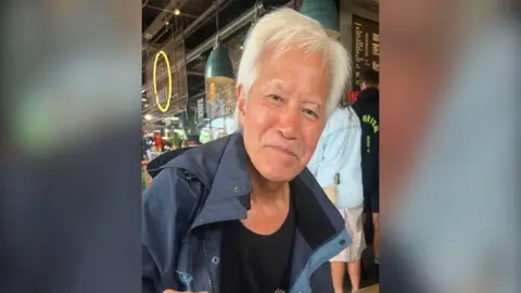 FAMILY HANDOUT Mr Fong a man with white hair and a moustache wears a navy coat as he sits in a cafe.