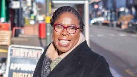 Labour Paulette Hamilton wearing a black coat and multi-colours scarf in a high street