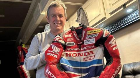 John McGuinness holding his red Honda Racing leathers
