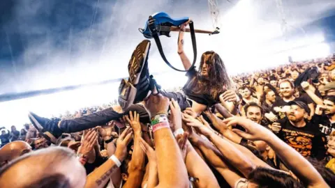 Jez Pennington A man crowdsurfing while holding up his guitar