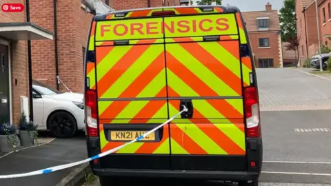 The back of a police van with yellow and orange chevrons and the word 'Forensics' across the top, parked in a housing estate with police tape stretching away from the back door