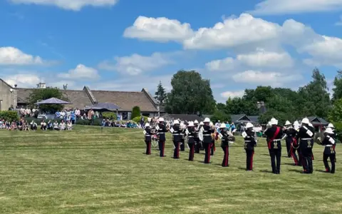 A crowd watches a brass band play on the lawn of a hospice in Wiltshire.