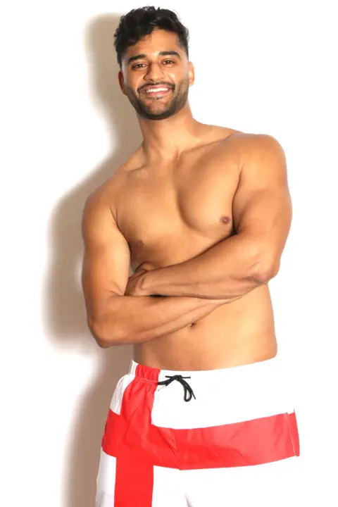 @mrenglanduk Bal is wearing shorts with the St George's cross on them. He is topless, folding his arms across his chest. He is and slim and toned and could pass for a Love Island contestant!