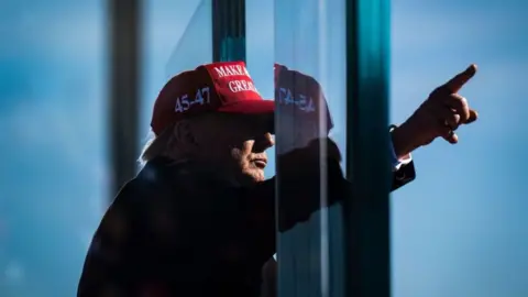 Trump points finger in the air while wearing a red "Make America Great Again" hat