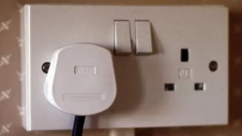 A white plug with a black flex is plugged into one side of a double socket