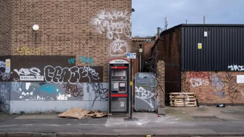 Graffiti covered street corner with rubbish strewn about outside an old industrial factory building in Birmingham