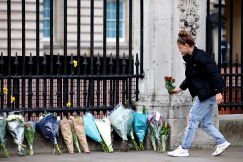 AFP A woman adds a bunch of flowers to a line of floral tributes against the railings at the front of Buckingham Palace