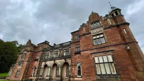 BBC A three-storey Keele University building. Trees and grass are to the far left of the photo.