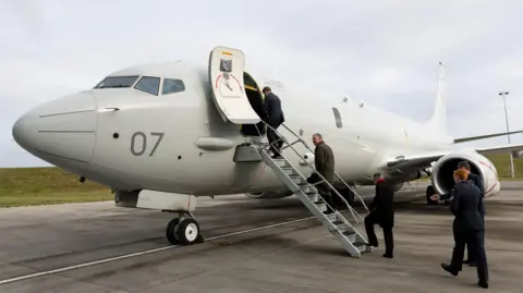 Five men in uniform are boarding a military jet plane