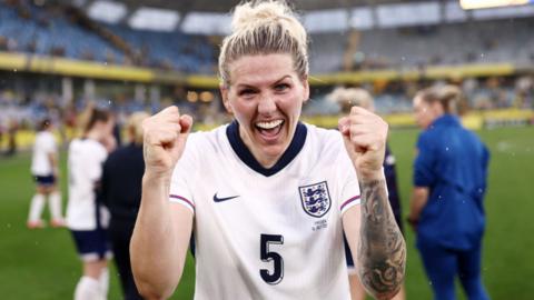 Millie Bright holding up two fists in a celebration on the pitch after the game