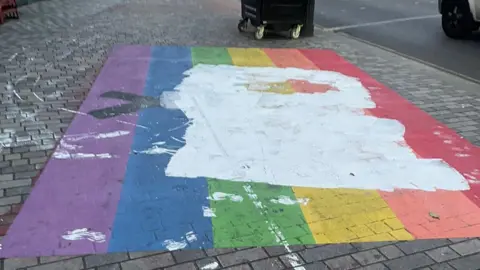 A rainbow flag painted on the pavement, covered in white paint