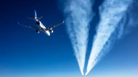 Airbus An Airbus A350 flying behind the contrail of another jet in blue skies