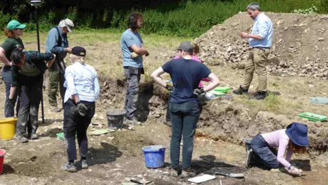 Nine people with buckets and tools working on an archaeological trench