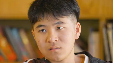 BBC Zhang Junjie speaking to the BBC indoors - he gazes intently at the reporter  and is dressed casually. He has short brown hair, slightly shaved at the sides.