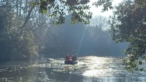 A small rubber boat with firemen inside on a lake in a park.