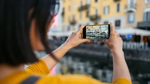 A woman holding her phone in front of her so she can film a canal in Milan