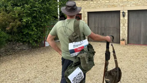 Philip Burlingham Philip with his back the camera on a driveway wearing his old army gear and a leather brimmed hat with a help for heroes sign on his back