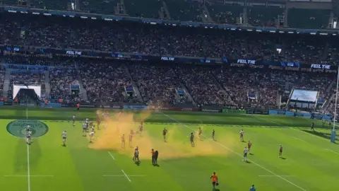 BBC Image showing orange powder spreading across air above the pitch