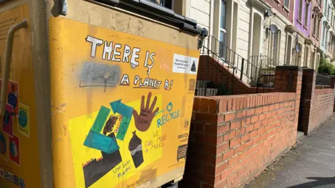 A recycling Bin that's been graffitied with slogans about climate and recycling on a street in St Pauls