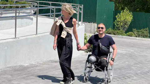 Olga Rudnieva Olga Rudnieva walks next to a ramp holding the hand of one of the amputees in her trauma centre - a man with a double leg amputation in a wheelchair