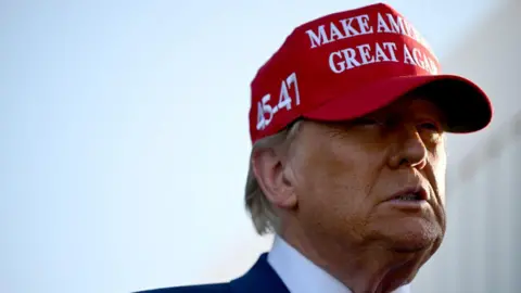 Donald Trump wearing a red baseball cap which reads "Make America Great Again" and has the numbers 45 and 47 embroidered on the side, referring to his previous tenure as the 45th US president and his forthcoming term as the 47th