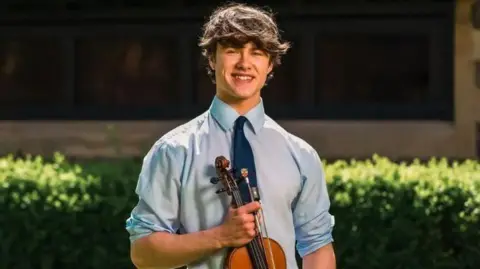 Anthony Knight holding his violin and smiling