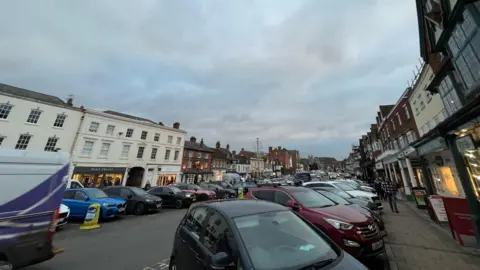 A view of the high street with lots of parked cars.