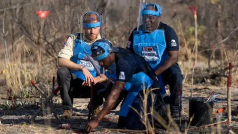 Reuters Britain's Prince Harry, Duke of Sussex, and Halo Regional Manager Jose Antonio watch as Mine Clearer Jorge Joao Cativa demonstrates mine clearing techniques during his visit to a working de-mining field with the HALO Trust in Dirico Province, Angola, September 27, 2019.