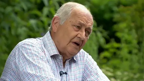 Henry Prince speaking to the BBC in 2014 on the 50th anniversary of the founding of the Red Arrows. He has grey hair and is wearing a chequered-patterned shirt.