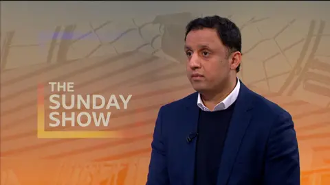 Anas Sarwar in The Sunday Show studio, wearing a a white shirt, dark blue jumper and jacket