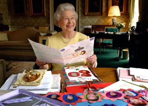 PA Media Queen Elizabeth II sits in the Regency Room at Buckingham Palace in London as she looks at some of the cards which have been sent to her for her 80th birthday