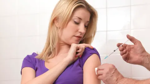 Woman receives flu vaccine jab in the top of her arm