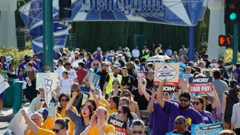 Hundreds of Disneyland workers are seen with signs protesting outside the park's gates 