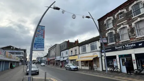 A general view of Freeman Street in Grimsby. Shops, including a Cooplands bakery and a butchers flank the road. 