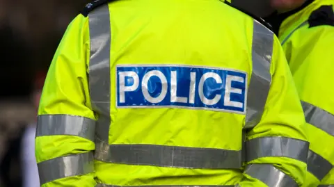 Close up of back of generic police officer who is wearing a high vis yellow jacket that says Police on with white lettering and blue background.