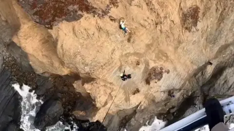 Man clinging to a cliff being rescued 