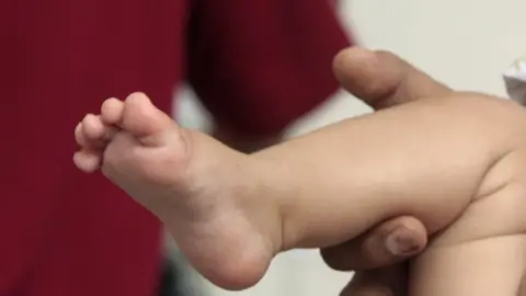 An adult holds a baby's foot