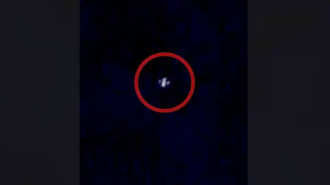 An image of an alleged drone caught on camera in the night sky above New Jersey. A red ring is around it