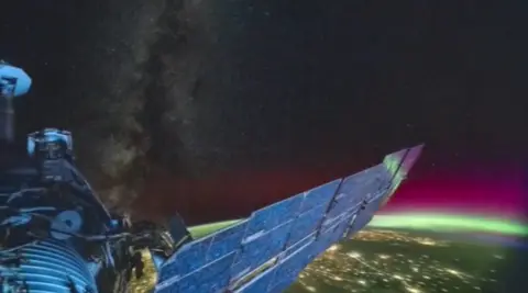 ISS orbiting over globe with green and purple lights shining over Earth