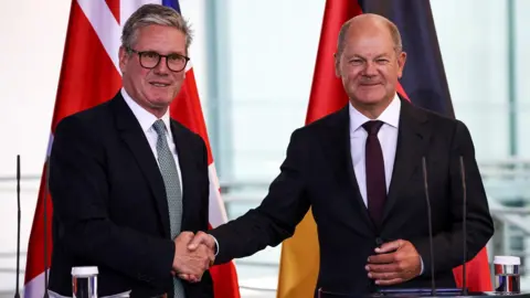 Prime Minister Sir Keir Starmer shakes hands with German Chancellor Olaf Scholz in front of UK and German flags at a news conference in Berlin