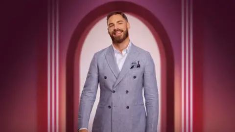 Publicity shot featuring Steven Smith in a grey jacket and white shirt smiling at the camera, framed by a pink archway