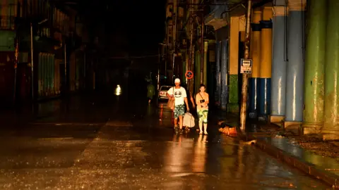 Three people walking down an empty road in complete darkness during the blackout